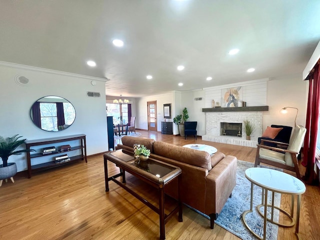 living room featuring an inviting chandelier, crown molding, a fireplace, and light hardwood / wood-style floors