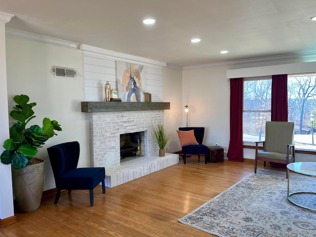 living room with hardwood / wood-style floors, crown molding, and a brick fireplace