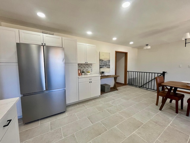 kitchen featuring decorative backsplash, stainless steel refrigerator, and white cabinets