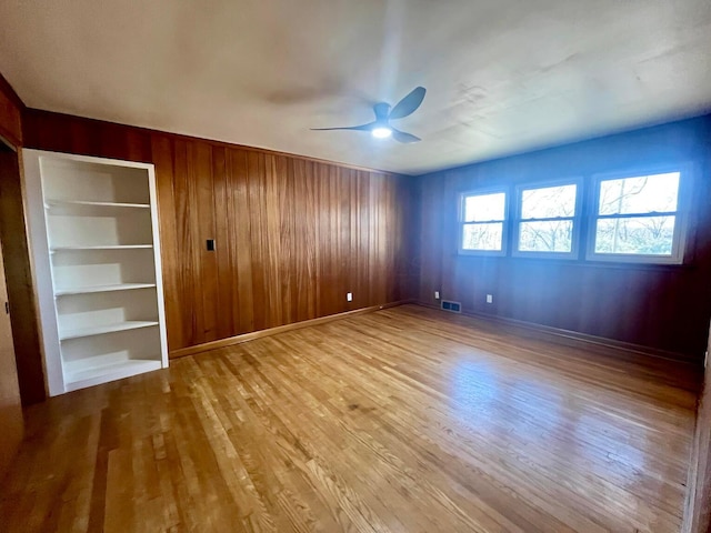 spare room featuring wooden walls, ceiling fan, and light wood-type flooring