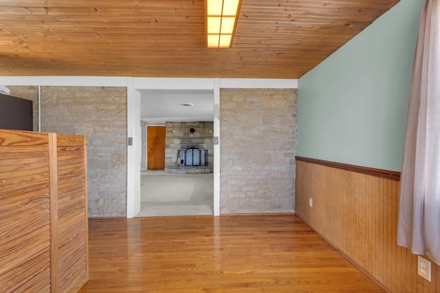 unfurnished room with a stone fireplace, wooden ceiling, wood walls, and light wood-type flooring