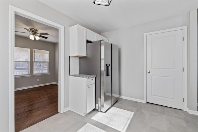 kitchen featuring light tile patterned floors, stainless steel fridge, ceiling fan, white cabinetry, and light stone counters