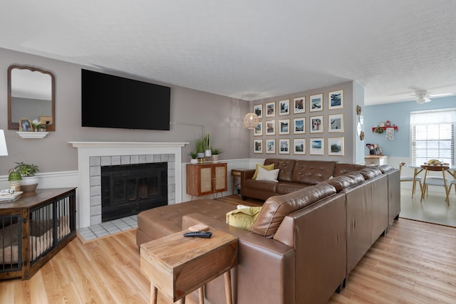 living room featuring light wood-type flooring, a tiled fireplace, a textured ceiling, and ceiling fan