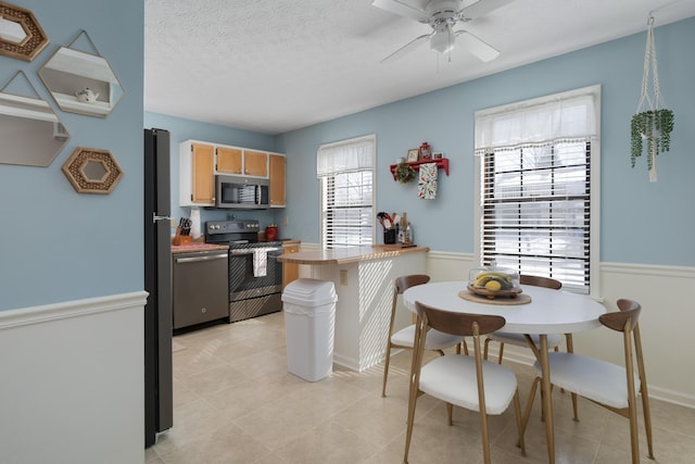 kitchen featuring tile counters, ceiling fan, a textured ceiling, appliances with stainless steel finishes, and a kitchen breakfast bar