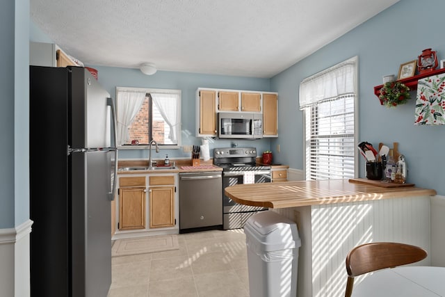 kitchen with light tile patterned floors, stainless steel appliances, a textured ceiling, and sink