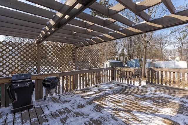 snow covered deck with area for grilling, a pergola, and a storage unit