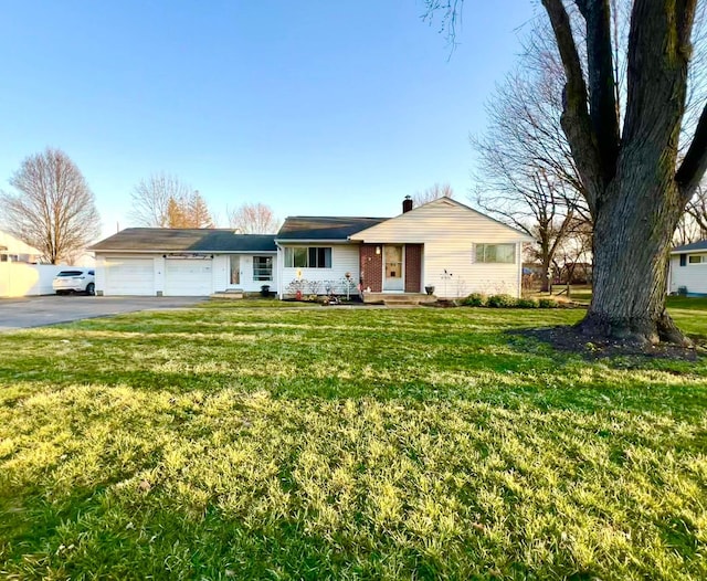 single story home featuring an attached garage, a chimney, a front lawn, aphalt driveway, and brick siding