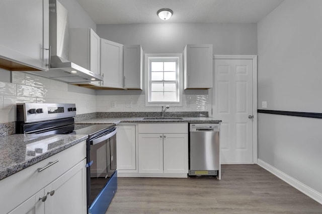 kitchen featuring sink, white cabinetry, appliances with stainless steel finishes, decorative backsplash, and wall chimney range hood