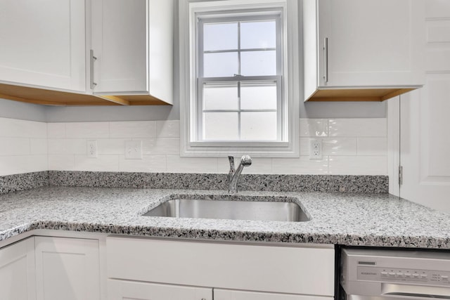 kitchen with sink, dishwashing machine, a healthy amount of sunlight, light stone countertops, and white cabinets