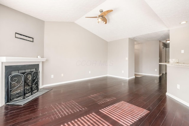 unfurnished living room with a fireplace with raised hearth, dark wood-type flooring, vaulted ceiling, ceiling fan, and baseboards