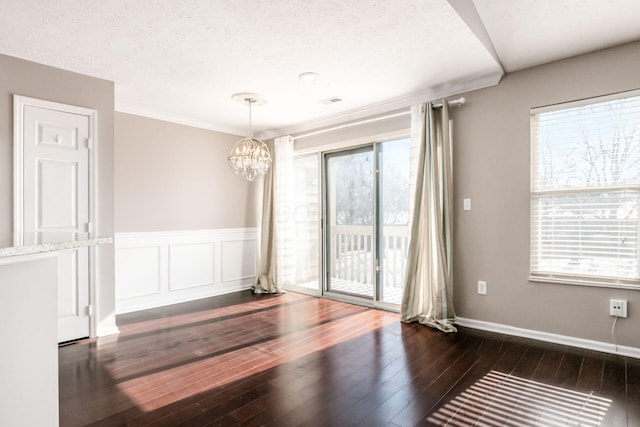 empty room featuring baseboards, wainscoting, dark wood-type flooring, a textured ceiling, and a chandelier