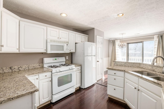 kitchen featuring white appliances, a sink, white cabinetry, light stone countertops, and pendant lighting