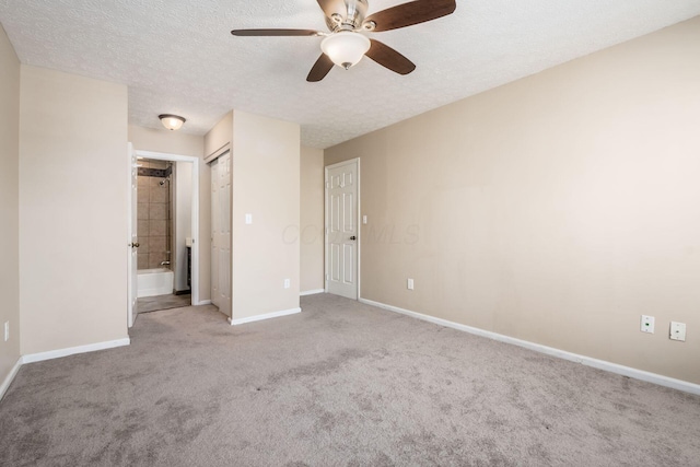 unfurnished bedroom featuring baseboards, light colored carpet, ceiling fan, ensuite bathroom, and a textured ceiling