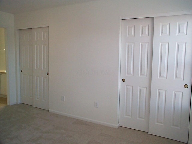 unfurnished bedroom featuring multiple closets, light colored carpet, and baseboards