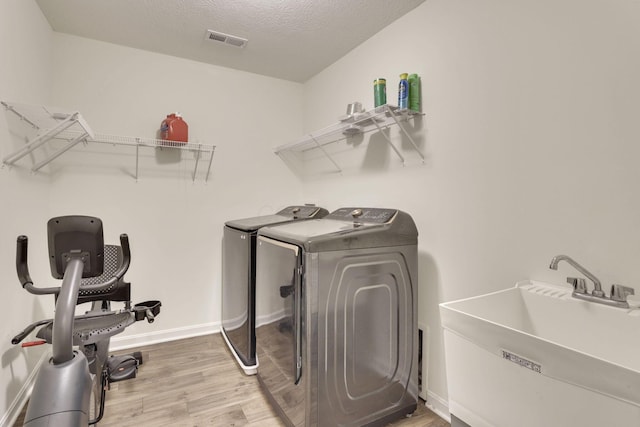 laundry area featuring sink, wood-type flooring, washing machine and dryer, and a textured ceiling