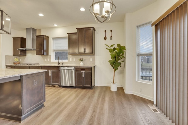 kitchen featuring decorative light fixtures, wall chimney range hood, light wood-type flooring, stainless steel appliances, and backsplash