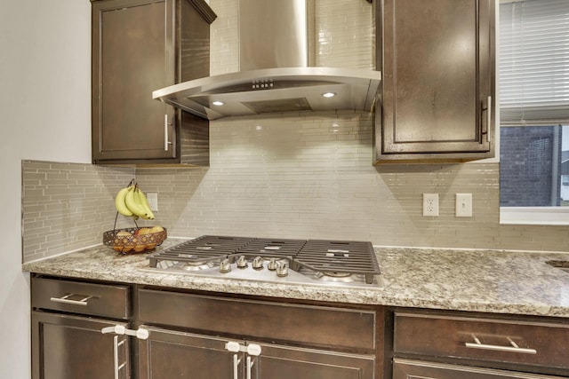 kitchen featuring stainless steel gas cooktop, decorative backsplash, dark brown cabinetry, and range hood