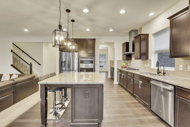 kitchen with sink, a breakfast bar, stainless steel appliances, a kitchen island, and wall chimney exhaust hood