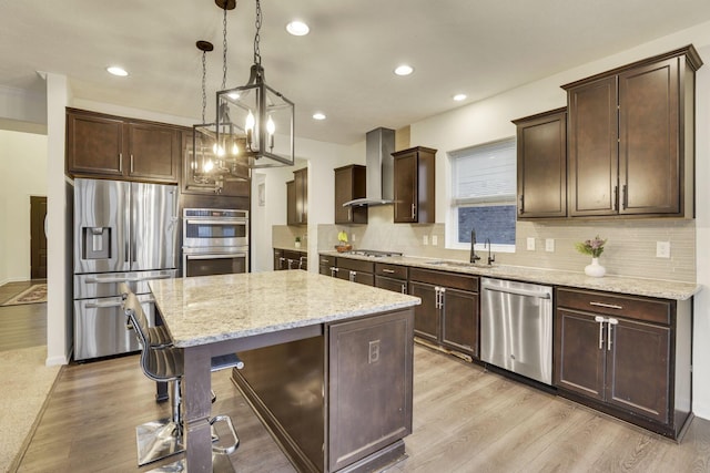 kitchen with wall chimney exhaust hood, sink, a center island, hanging light fixtures, and stainless steel appliances