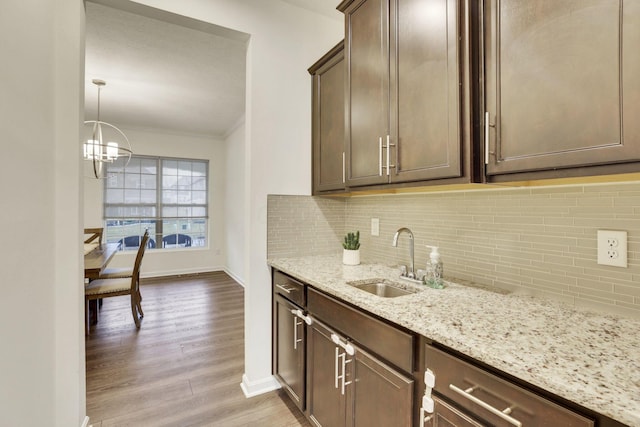 kitchen with sink, dark brown cabinetry, tasteful backsplash, light stone countertops, and light hardwood / wood-style floors