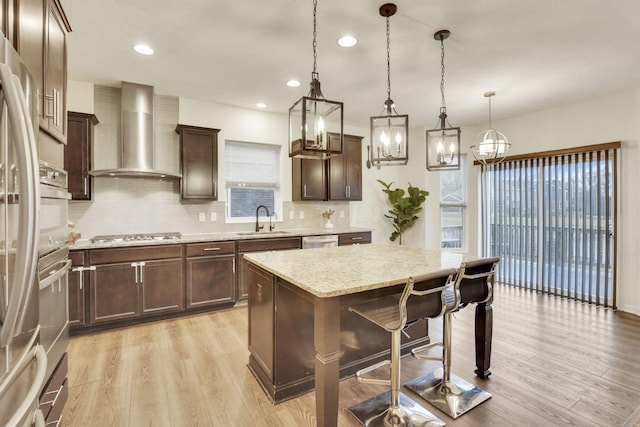 kitchen with wall chimney exhaust hood, sink, decorative light fixtures, a center island, and light wood-type flooring