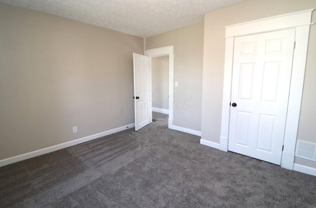 unfurnished bedroom featuring dark colored carpet, a textured ceiling, and a closet