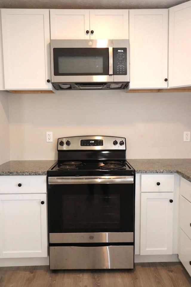 kitchen with white cabinetry, hardwood / wood-style flooring, stainless steel appliances, and dark stone countertops