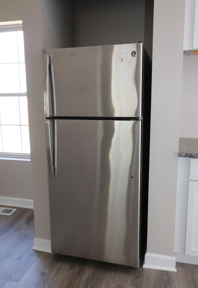 kitchen featuring a healthy amount of sunlight, stainless steel refrigerator, white cabinets, and stone countertops