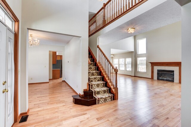 entryway with a tile fireplace, light hardwood / wood-style flooring, an inviting chandelier, and a high ceiling