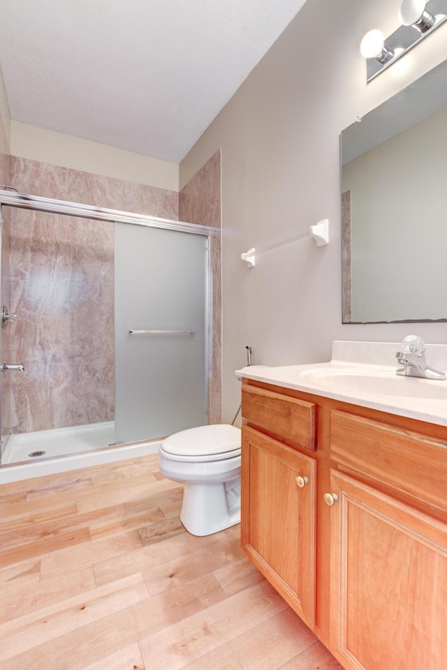 bathroom featuring toilet, vanity, hardwood / wood-style floors, and a shower with door