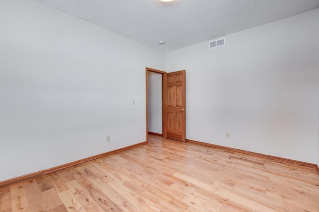 empty room with light wood-type flooring and a textured ceiling