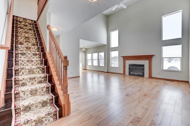 unfurnished living room featuring a fireplace, light hardwood / wood-style floors, a high ceiling, and a textured ceiling