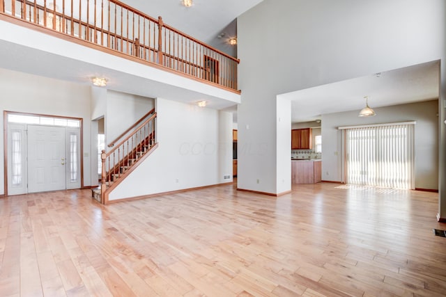 unfurnished living room with light wood-type flooring and a towering ceiling