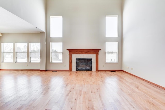 unfurnished living room with a tile fireplace, a towering ceiling, and light wood-type flooring