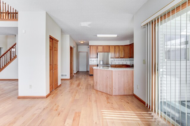 kitchen with light hardwood / wood-style flooring, stainless steel fridge with ice dispenser, and decorative backsplash