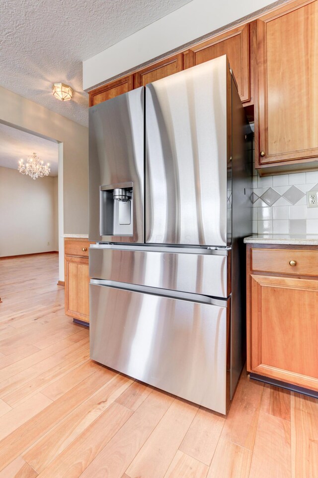 kitchen featuring light hardwood / wood-style floors, tasteful backsplash, a textured ceiling, and stainless steel fridge