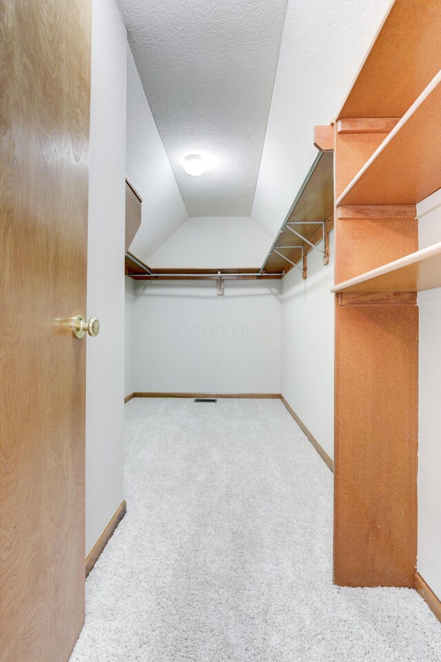 walk in closet with light carpet and lofted ceiling