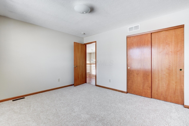 unfurnished bedroom featuring a textured ceiling, light carpet, and a closet