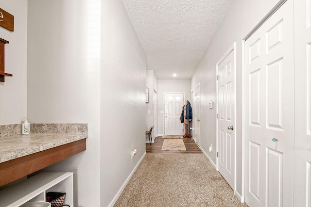 hall featuring baseboards, a textured ceiling, and light colored carpet