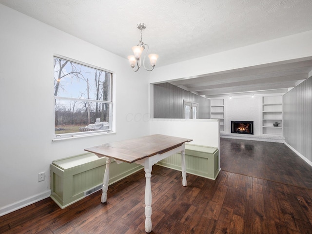 dining area featuring a notable chandelier, breakfast area, dark wood-type flooring, a textured ceiling, and built in shelves