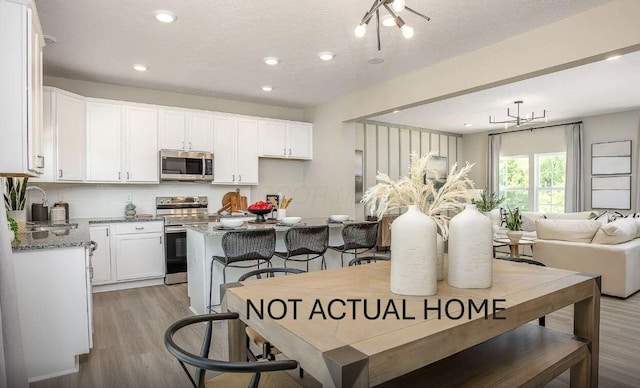 dining space featuring a kitchen island, a breakfast bar, white cabinetry, light stone counters, and light hardwood / wood-style floors