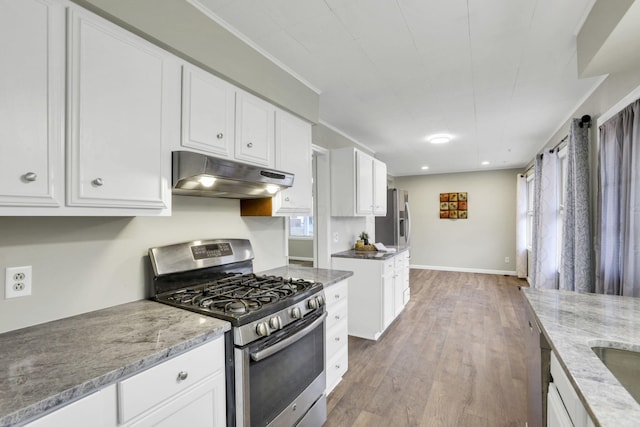 kitchen with stainless steel appliances, white cabinetry, wood-type flooring, and light stone counters