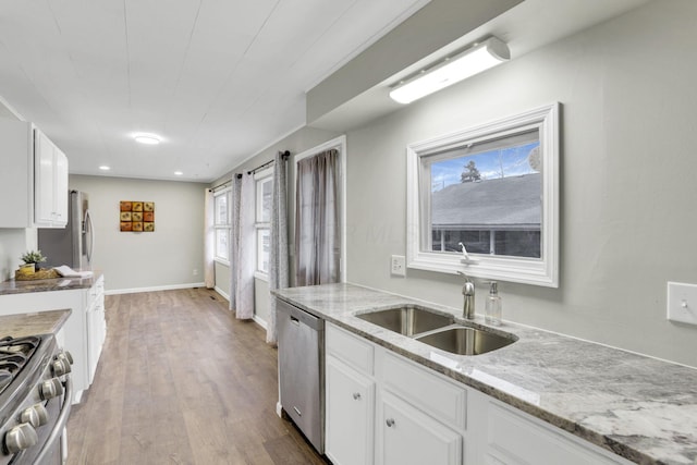 kitchen with sink, light wood-type flooring, stainless steel appliances, light stone countertops, and white cabinets