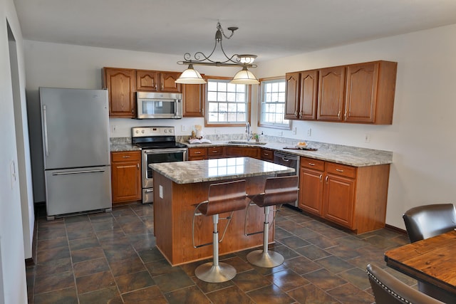 kitchen featuring sink, light stone counters, decorative light fixtures, appliances with stainless steel finishes, and a kitchen island