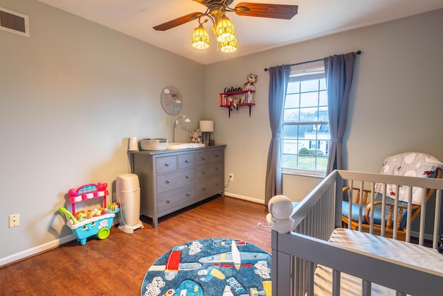 bedroom with hardwood / wood-style flooring, ceiling fan, and a crib