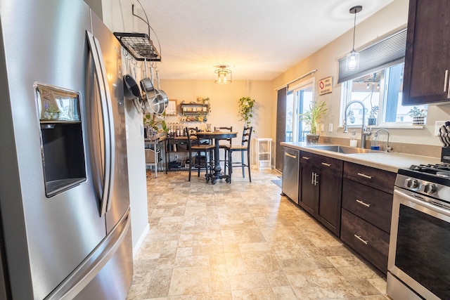 kitchen with appliances with stainless steel finishes, sink, pendant lighting, and dark brown cabinetry