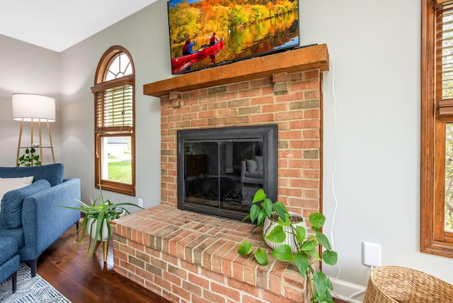 living area featuring baseboards, a brick fireplace, and dark wood-type flooring