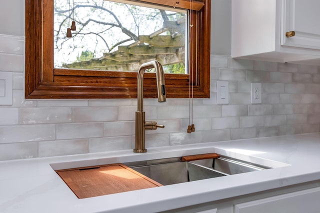 room details with decorative backsplash, light countertops, a sink, and white cabinetry
