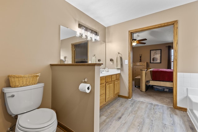 bathroom with hardwood / wood-style flooring, toilet, a tub to relax in, ceiling fan, and vanity