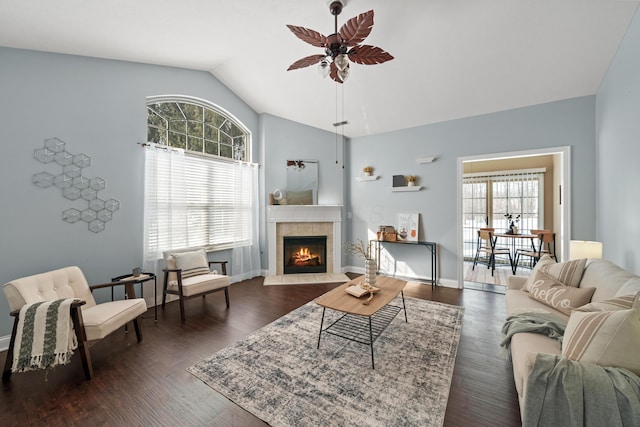 living area featuring baseboards, a ceiling fan, a tile fireplace, dark wood-type flooring, and vaulted ceiling